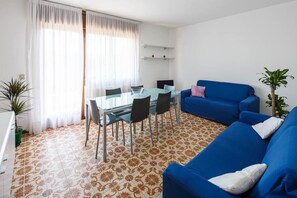 A modern living room with a glass dining table, blue sofa, and patterned floor tiles.