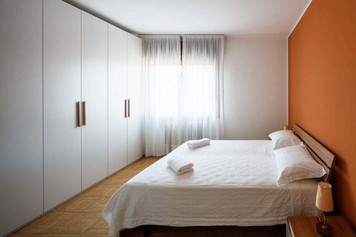 Ein Hotelzimmer mit Bett, Nachttisch, Lampe und einem Fenster mit Vorhängen.