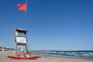 A lifeguard station with a red flag, a lifebuoy, and a beach in the background.