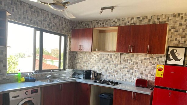 Una cocina pequeña con armarios de madera, lavadora, cocina a gas y refrigerador rojo.
