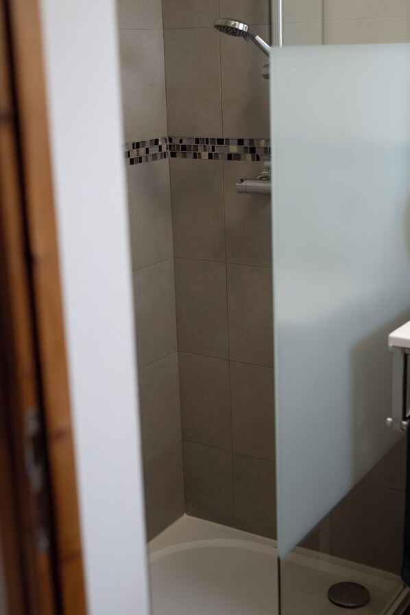 A shower with a tiled wall and a showerhead.