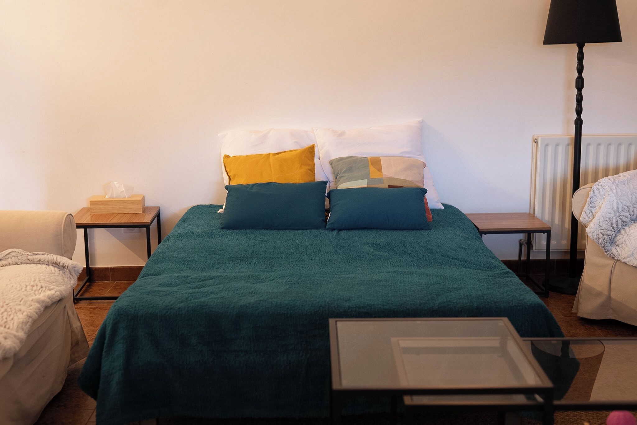 A bedroom with a bed, two bedside tables, a lamp, a radiator, and a small table.