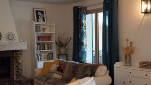 Ein Wohnzimmer mit Kamin, einer Couch, einem Bücherregal und einem Fenster mit Vorhängen.