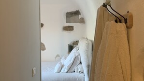 Et soveværelse med en seng, hvide sengetøj, trægulv og et håndklæde hængende på en krog.