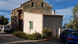 A stone building with a sloped roof, a small porch, and a vehicle parked in front. - Small apartment 15 minutes from Saint Florent overlooking CAP CORSICA (Santo-Pietro-di-Tenda)