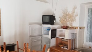 A compact kitchen with wooden cabinets, a dining table with chairs, a refrigerator, a microwave, and a television. - Small apartment 15 minutes from Saint Florent overlooking CAP CORSICA (Santo-Pietro-di-Tenda)