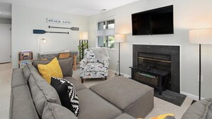 A living room with a grey sofa, patterned armchair, and a fireplace. - Coastal Chic 2BR Condo w/ Community Pool, Walk to Restaurants (Rehoboth Beach)