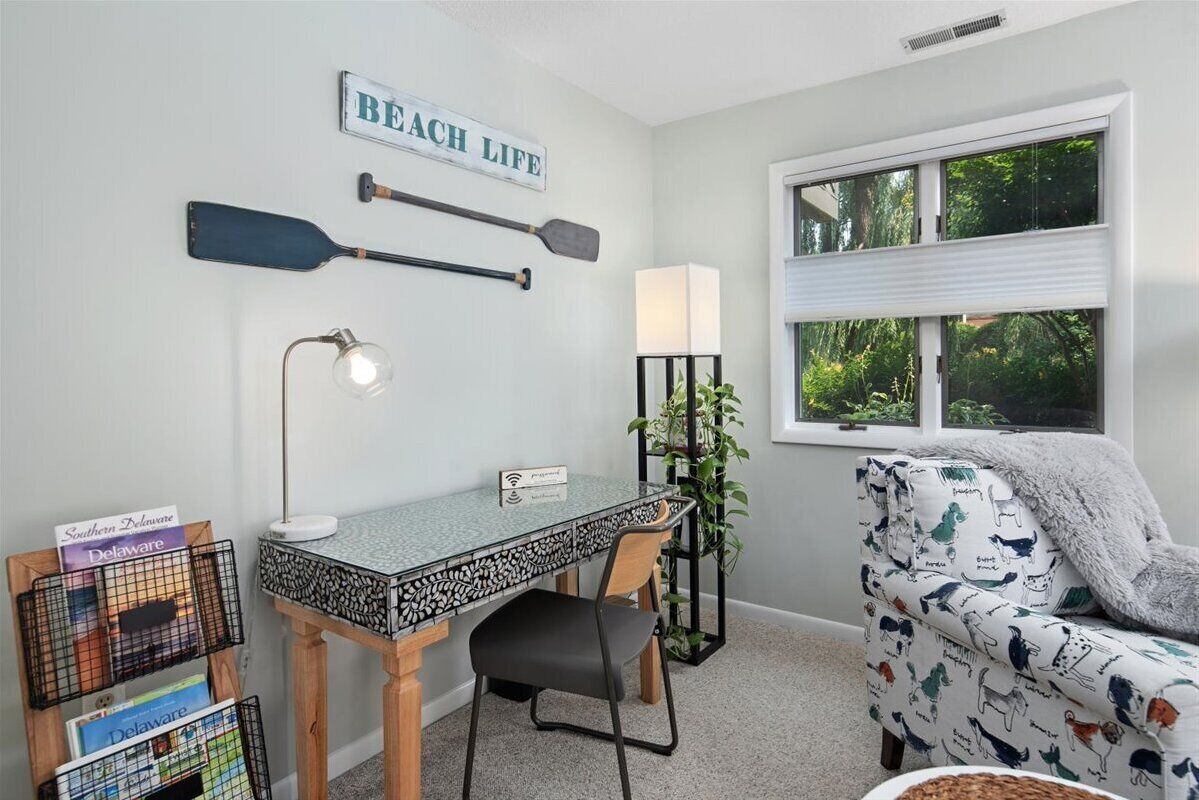 A cozy room with a desk, chair, and a couch. There is a sign on the wall that says "BEACH LIFE".