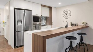 Eine moderne Küche mit einem Edelstahl-Kühlschrank, einem eingebauten Backofen und einer Holzinsel mit Barhocker.