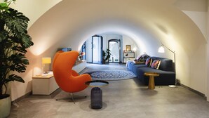 A modern living room with a curved ceiling, a blue sofa, an orange chair, a round coffee table, and a potted plant.