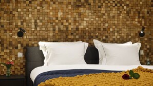 A neatly made bed with white linens and a blue accent throw, set against a wooden mosaic wall.