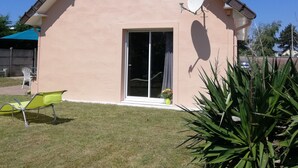 A single-story house with a sloped roof, a satellite dish, a sliding glass door, and a small garden area with a lawn and a potted plant. - House 42 m2, 200 m from the sandy beach, with enclosed garden and parking. (Portbail)