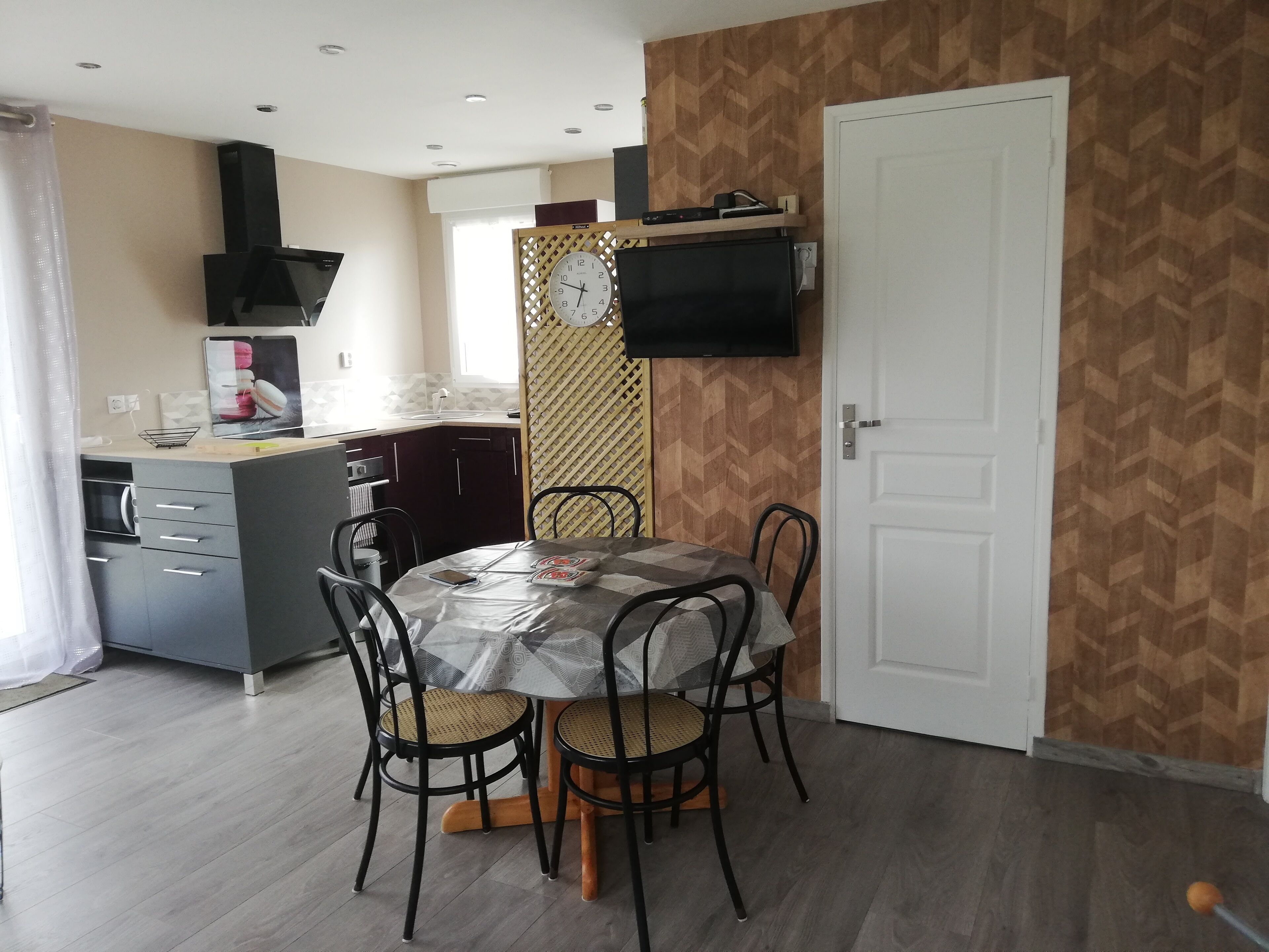 Une cuisine compacte avec un coin repas, un téléviseur fixé au mur et un mur décoré d’un motif.