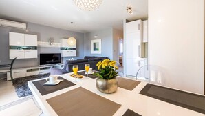 A modern living room with a dining area, a sofa, a TV, and a vase with flowers. - Charming and Stunning 2bedroom Apartment Cavtat (Konavle)