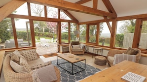Un espacio habitable acogedor y de concepto abierto con muebles de mimbre, una mesa de madera y ventanas amplias que ofrecen vistas al jardín.
