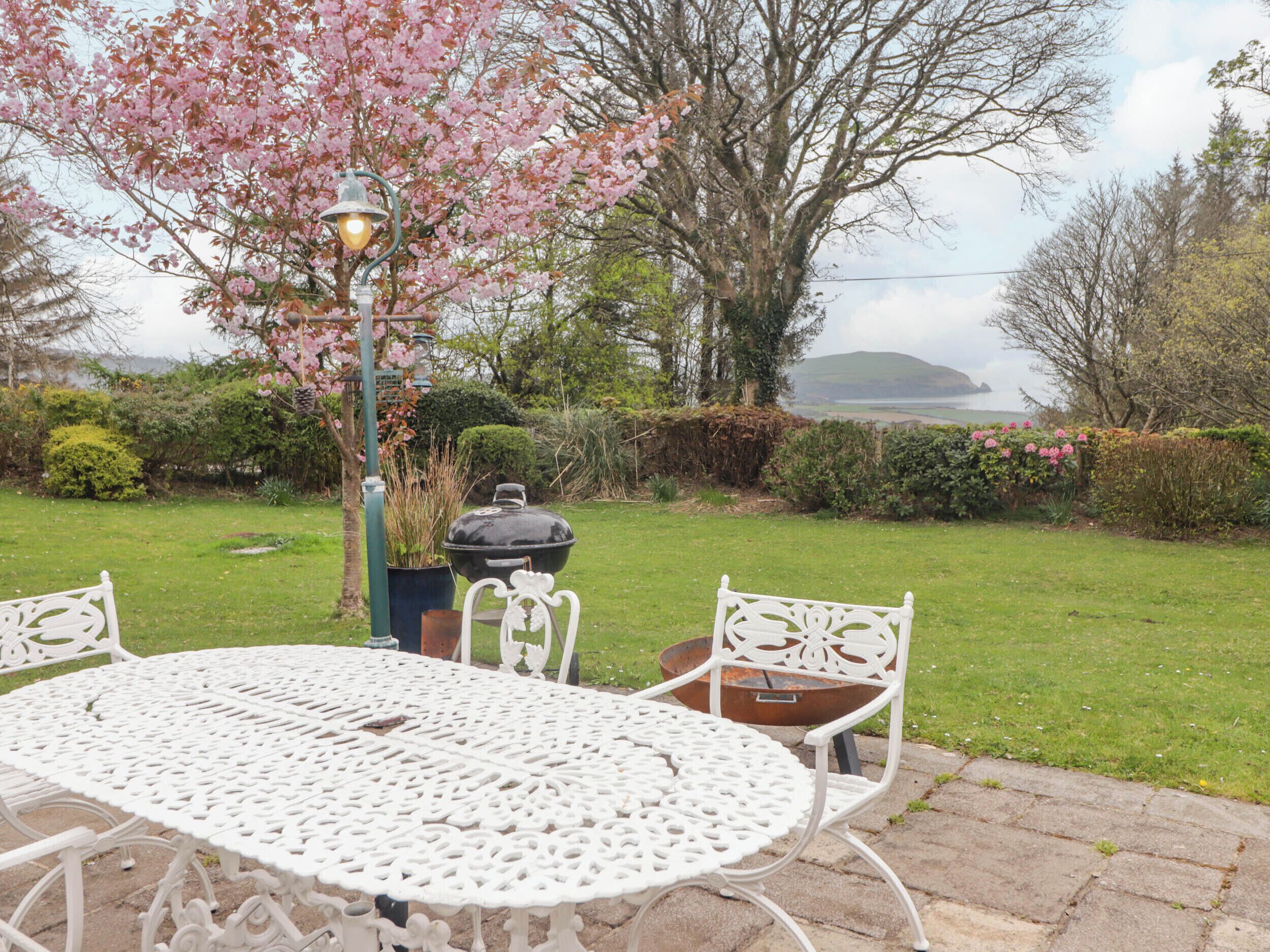 Une terrasse de jardin avec une table et des chaises en métal blanc, une lampe décorative et un barbecue.