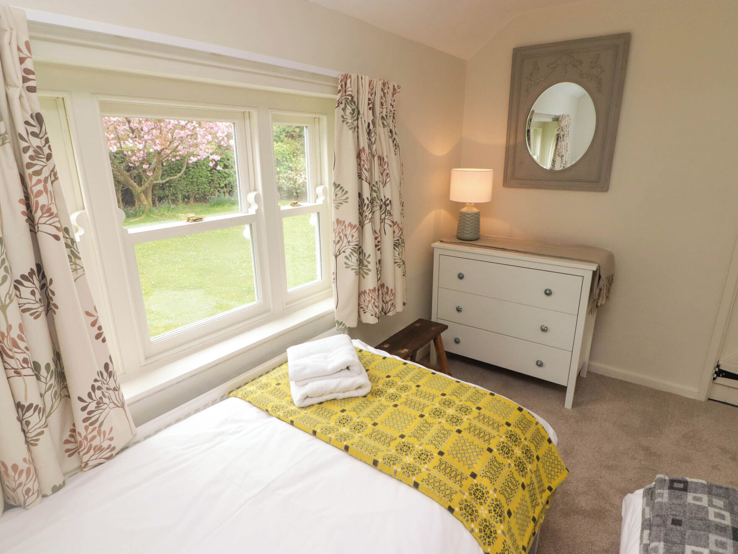 A bedroom with a bed, a bedside table with a lamp, a dresser, and a window with curtains.