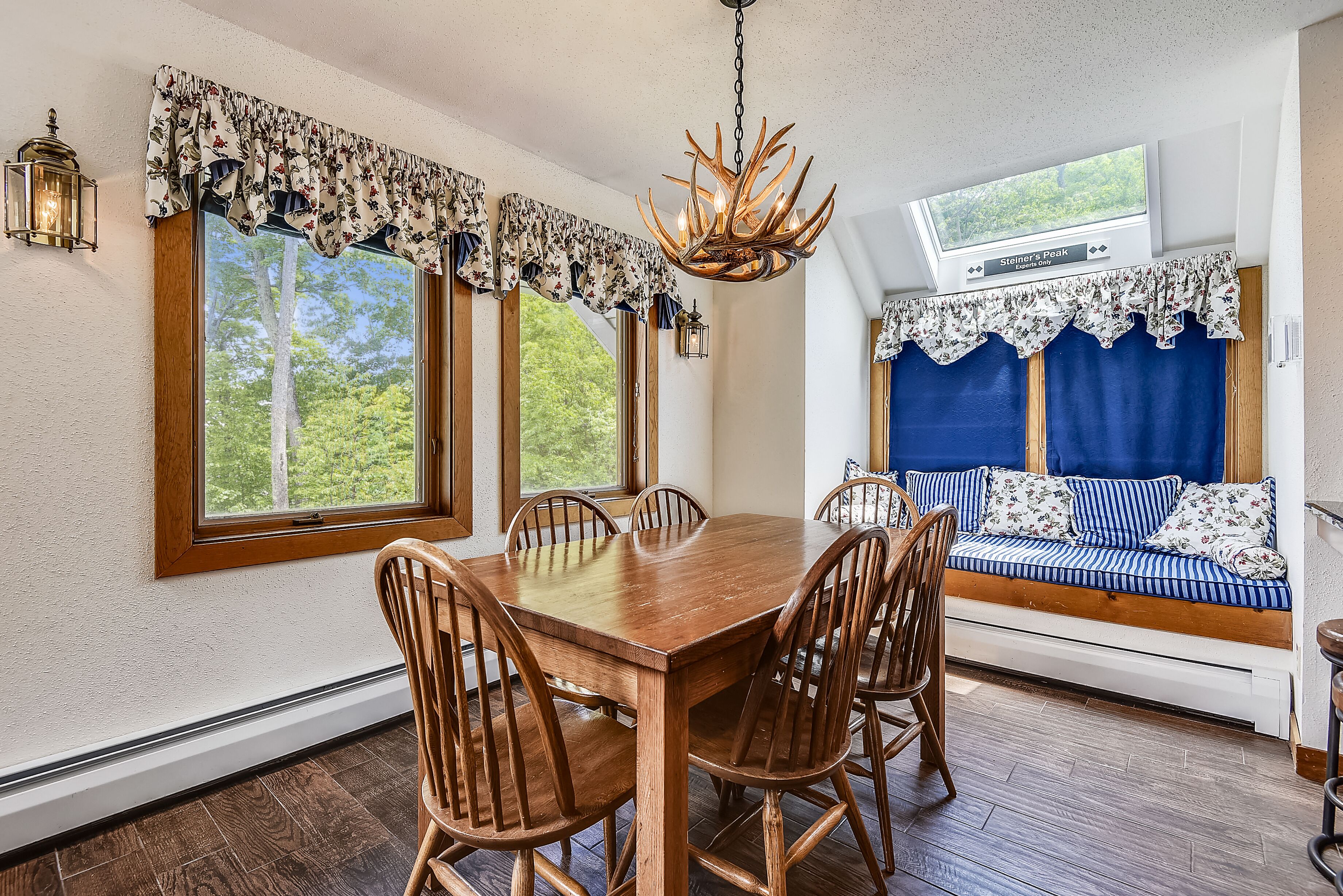 Un coin repas avec une table et des chaises en bois, un lustre et une vue sur l’extérieur grâce à de grandes fenêtres.