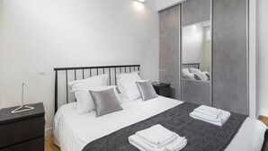 A modern bedroom with a large bed, a nightstand, a mirror, and a wardrobe. - 4-room apartment with 3 bedrooms in Montmartre A/C near the metro (Paris)