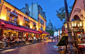 A cobblestone street lined with cafes and restaurants, including 'Au Cadet de Gascogne'. - 4-room apartment with 3 bedrooms in Montmartre, with air conditioning, near the subway (Paris)