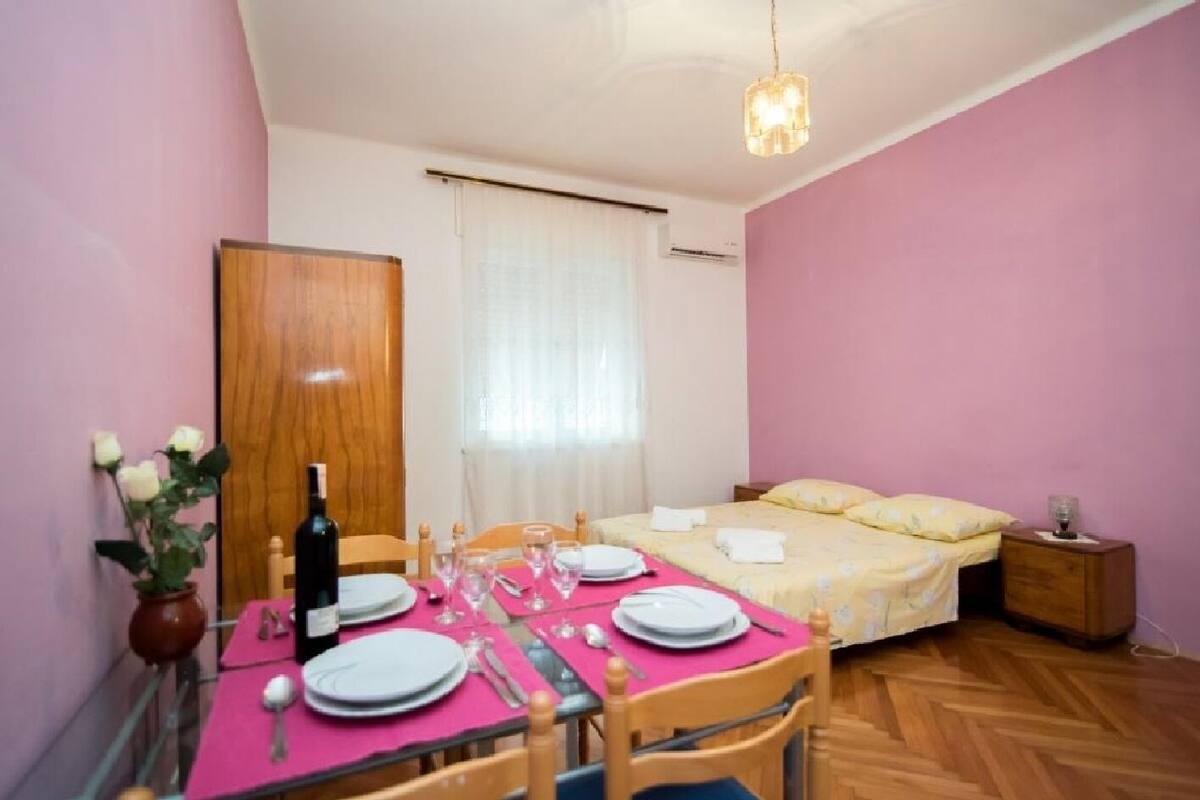 A room with a dining table set for four, a bed with a yellow bedspread, and a wooden floor.