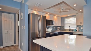 A modern kitchen with stainless steel appliances, a large island, and a ceiling fan.
