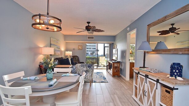A modern living room with a dining area, featuring a ceiling fan, a large window, and a view of the city.