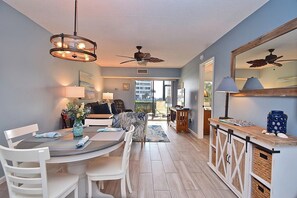 A modern living room with a dining area, featuring a ceiling fan, a large window, and a view of the city. - Waterfront on Turtle Beach Inlet - Ground Floor, Fish & Swim Steps From Your Door #19 (Siesta Key)