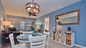 A dining area with a round table, white chairs, a chandelier, and a blue wall with a mirror.