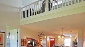 Un salón amplio con techo alto, una zona de comedor y una escalera que conduce a un nivel superior.