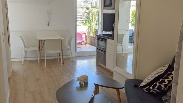 A compact living space with a kitchenette, a dining area with a table and chairs, and a sofa with patterned cushions. - La terrasse de Carras (Nice)