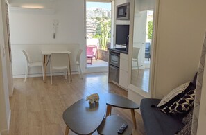 Un espacio habitable compacto con kitchenette, una zona de comedor con mesa y sillas, y un sofá con cojines estampados.