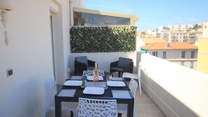 A balcony with a table set for two, white chairs, and a green wall. - La terrasse de Carras (Nice)