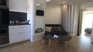 A modern kitchen with a microwave, oven, and a counter with bottles. There is a sofa with cushions and a small table with a figurine. - La terrasse de Carras (Nice)