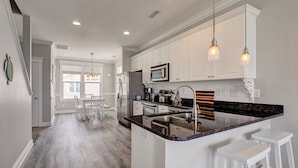 A modern kitchen with white cabinetry, a granite countertop, and pendant lighting. - 3 Bedroom Townhome in Surf City (Surf City)