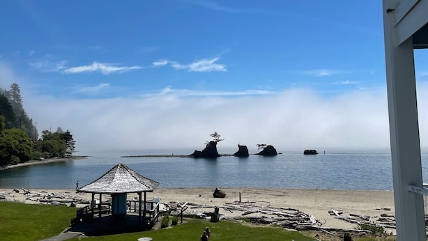 Un quiosco con vista a una playa, con afloramientos rocosos en la distancia y un cielo despejado.