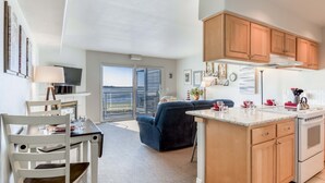 Una cocina moderna con armarios de madera, un comedor con mesa y sillas blancas, y un amplio ventanal con vistas al mar.