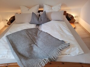 Una cama con ropa de cama blanca, un plaid gris y un cabecero de madera.