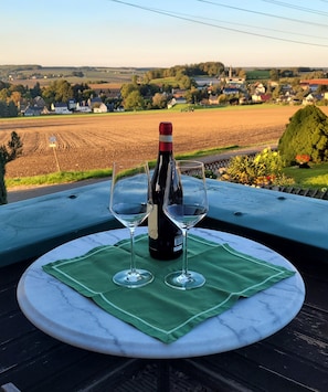 A table with a bottle of wine and two glasses on a green cloth, overlooking a rural landscape. - Apartment "Weitblick" Greiz in the Vogtland for max. 6 people  (Greiz)