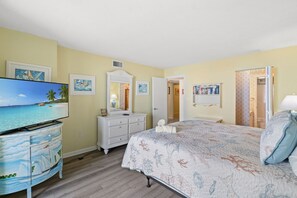 A bedroom with a bed, a dresser, a television, and a door leading to another room.