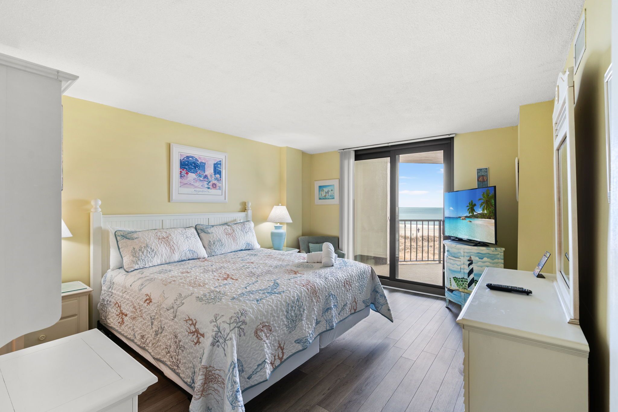 Un dormitorio con cama, mesitas de noche, escritorio, televisor y balcón con vistas.