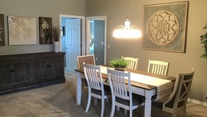 Un comedor con mesa de madera y sillas blancas, una araña y una gran pieza decorativa en la pared.
