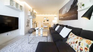 A modern living room with a flat-screen TV, a black sofa, a coffee table, and a large painting on the wall.