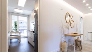 A modern kitchen with a dining area, white walls, and a view of the outside.