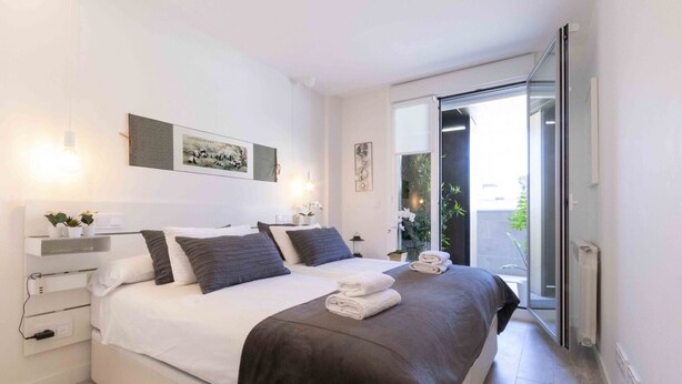 A modern bedroom with a large bed, bedside tables, and a sliding glass door leading to a balcony.