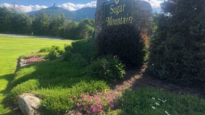 A stone sign with "Sugar Mountain" written on it, surrounded by green grass and bushes. - The Hideaway at Oma's Meadow (Sugar Mountain)