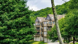 A multi-story building with balconies, surrounded by lush greenery and trees. - The Hideaway at Oma's Meadow (Sugar Mountain)