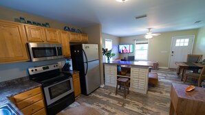 A kitchen with wooden cabinets, stainless steel appliances, a wooden dining table, and a television. - Fairfield Farm Cottage Dog Horse Welcome EV Charger 1Gig WI-FI Best HOST 21-2023 (Fairhope)