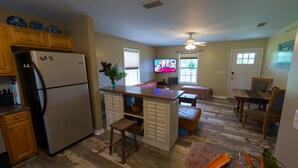A kitchen with a refrigerator, wooden cabinets, a dining area with a table and chairs, and a television. - Fairfield Farm Cottage Dog Horse Welcome EV Charger 1Gig WI-FI Best HOST 21-2023 (Fairhope)