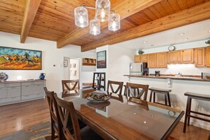 A spacious kitchen with wooden cabinets, a dining area with a glass table, and a ceiling with exposed beams. - Riverside Dream | Short Walk to Main Street & Hike (Telluride)